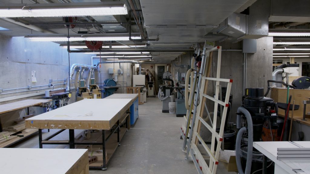Photo of woodshop, Gund L35, taken from Project Room, showing worktables, panel saw, downdraft table, and sanding equipment.