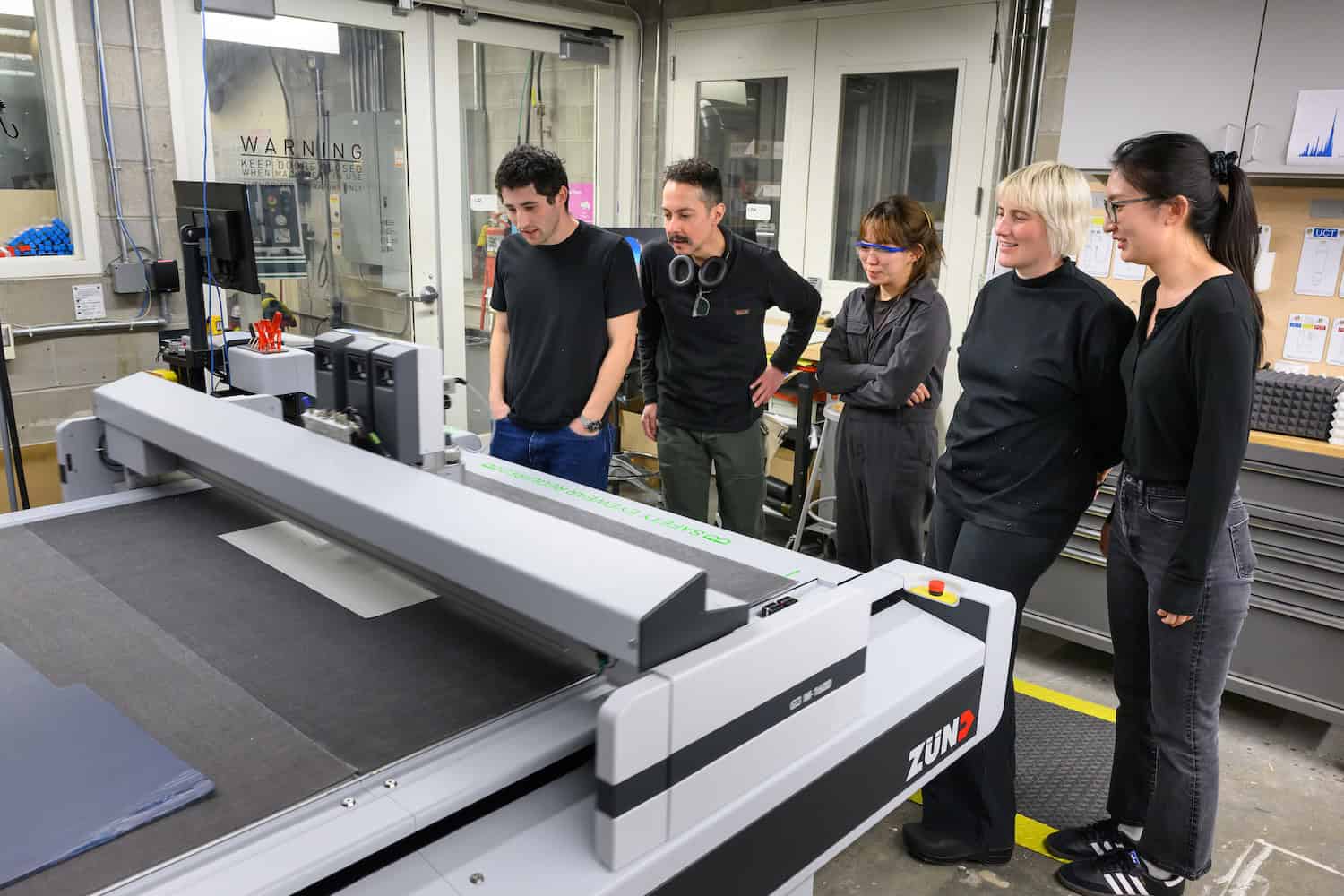 Five people gather around a Zund cutter to watch it.