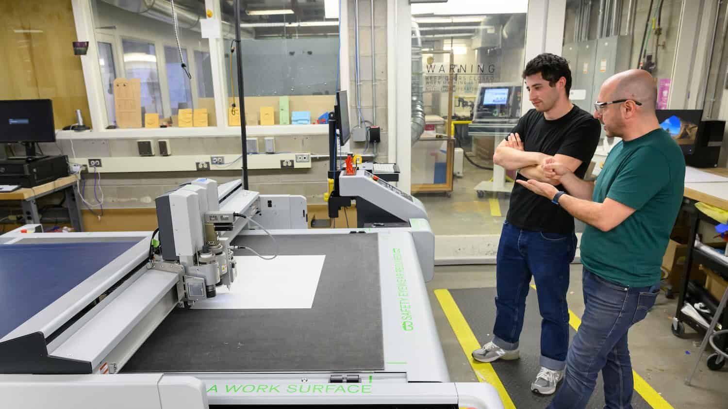 Two people watch a Zund cutter as is working.