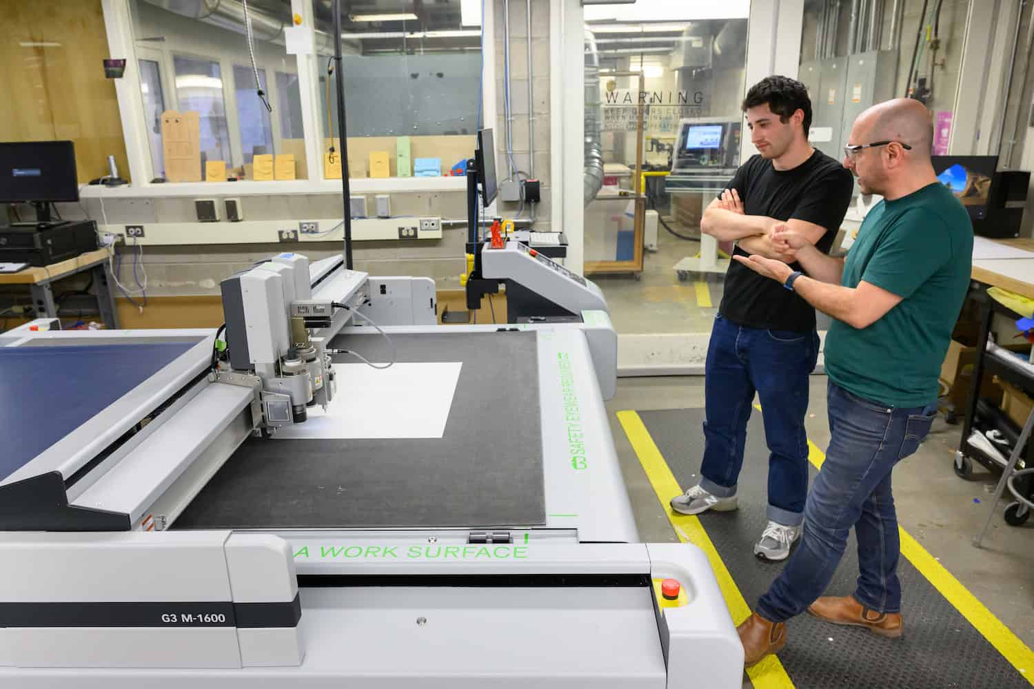 Two people watch a Zund cutter as is working.