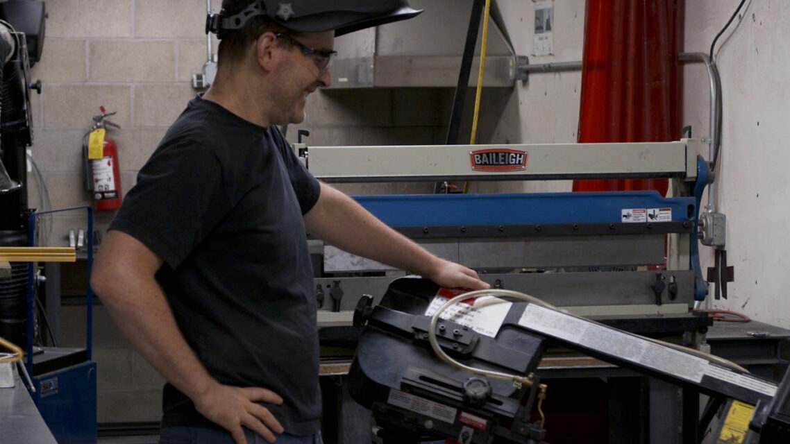 Photo of Burton, Lab Staff, using horizontal bandsaw in the Metal Shop, room L31A of Gund Hall Fabrication Lab.