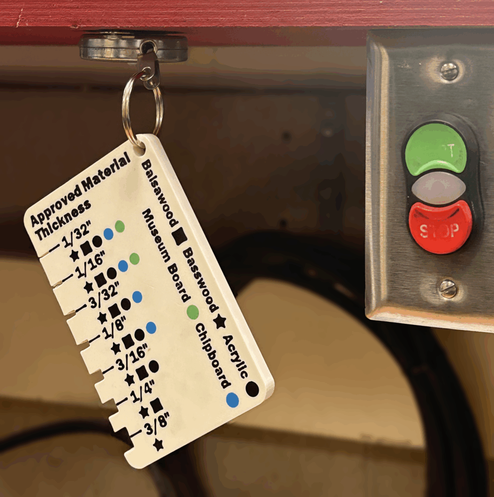 3D printed gauge for material types and thicknesses, suspended next to start/stop button for laser cutter.